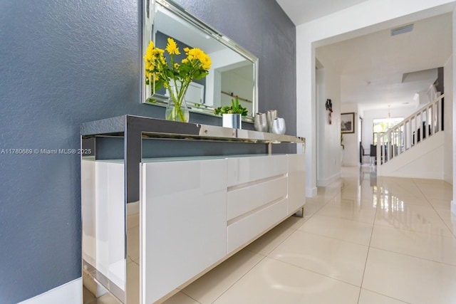 interior space featuring tile patterned flooring, visible vents, stairway, a textured wall, and a notable chandelier
