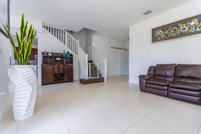 living room featuring visible vents, baseboards, light tile patterned floors, a barn door, and stairway