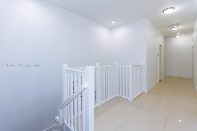 hall with visible vents, baseboards, an upstairs landing, and tile patterned flooring