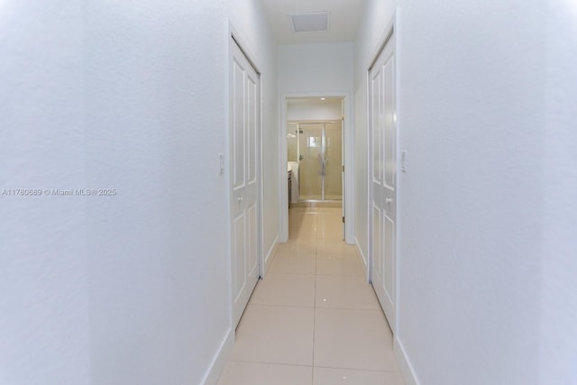 hallway with visible vents, baseboards, and light tile patterned flooring