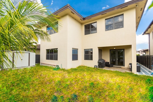 back of house with stucco siding, fence private yard, a lawn, a patio, and french doors