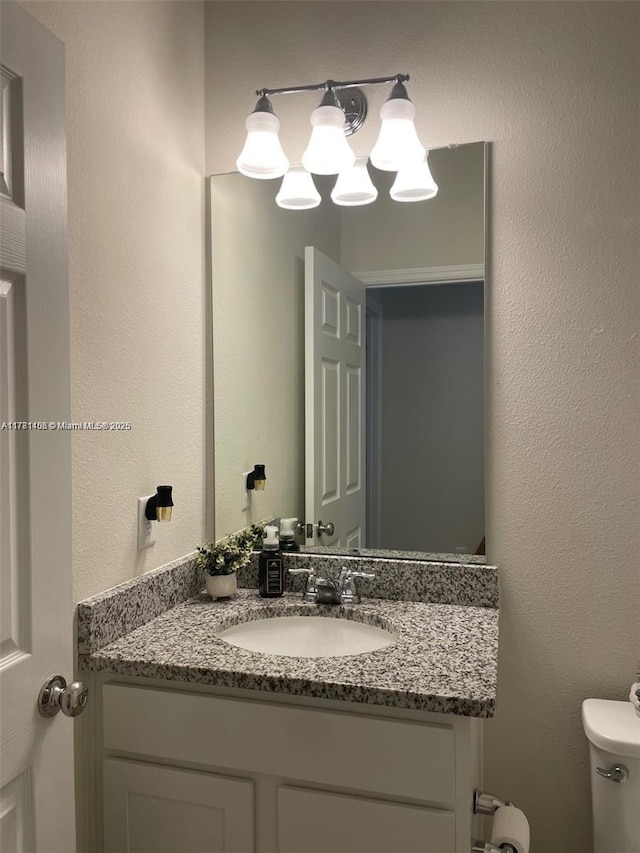 bathroom with toilet, vanity, and a textured wall
