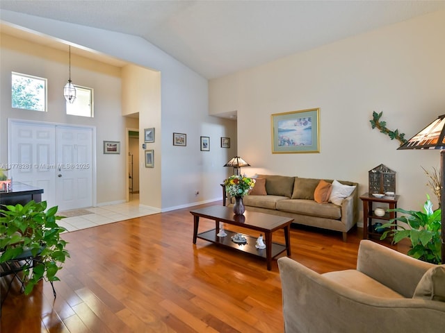 living area featuring high vaulted ceiling, light wood finished floors, and baseboards