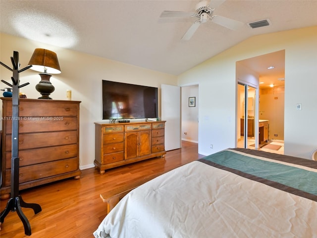 bedroom with visible vents, baseboards, light wood-style floors, ensuite bath, and vaulted ceiling