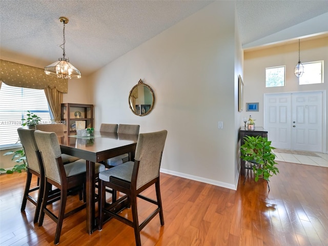 dining area featuring light wood finished floors, a notable chandelier, vaulted ceiling, and a textured ceiling