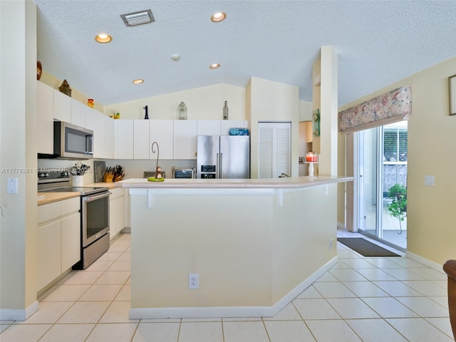 kitchen with light tile patterned floors, white cabinets, appliances with stainless steel finishes, and lofted ceiling