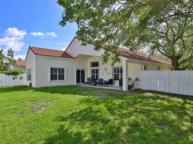rear view of house featuring a tiled roof, a lawn, fence, a patio, and stucco siding