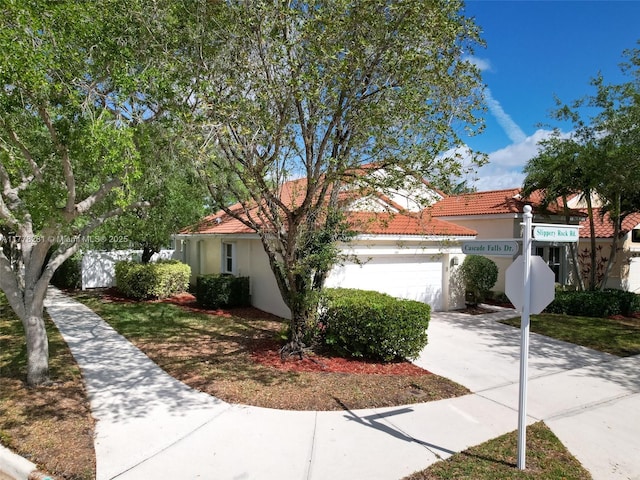 view of front of house with an attached garage, a tiled roof, driveway, and stucco siding