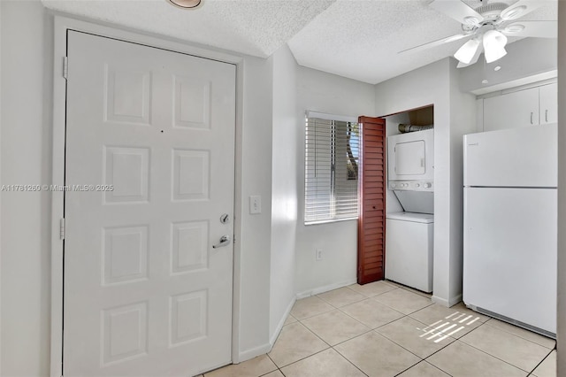 kitchen with freestanding refrigerator, a textured ceiling, stacked washer and dryer, a ceiling fan, and light tile patterned flooring