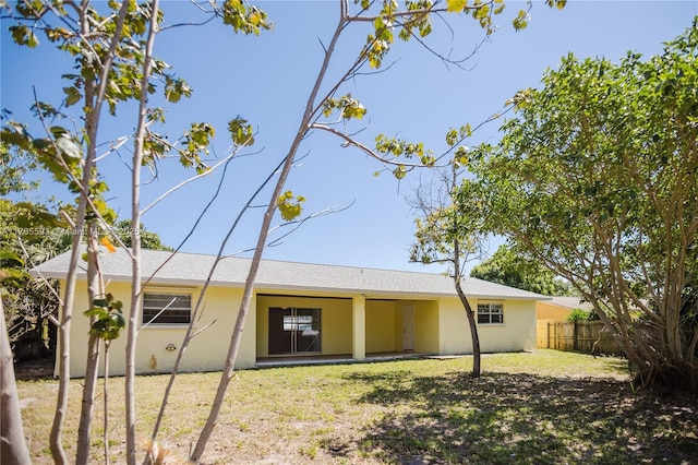 rear view of house with fence, a lawn, and stucco siding