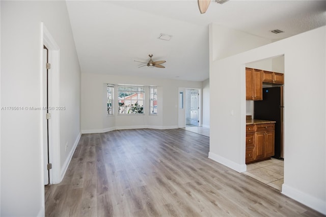 unfurnished living room with visible vents, baseboards, a ceiling fan, light wood-style floors, and vaulted ceiling