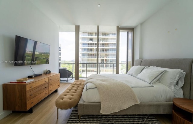 bedroom with floor to ceiling windows, light wood-style floors, and multiple windows