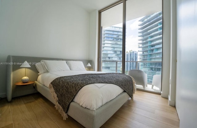 bedroom featuring a view of city, wood finished floors, and a wall of windows