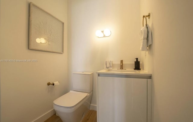 bathroom with wood finished floors, vanity, toilet, and baseboards