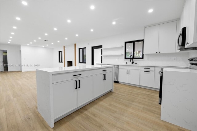 kitchen with light wood-type flooring, open shelves, a kitchen island, appliances with stainless steel finishes, and a sink