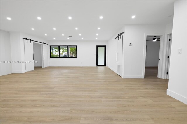 empty room featuring recessed lighting, a barn door, and light wood-style flooring