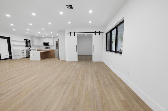 unfurnished living room with visible vents, recessed lighting, a barn door, and light wood-style floors