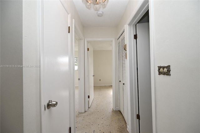 hall featuring baseboards and light speckled floor