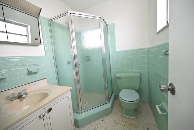 bathroom with a stall shower, vanity, tile walls, speckled floor, and toilet