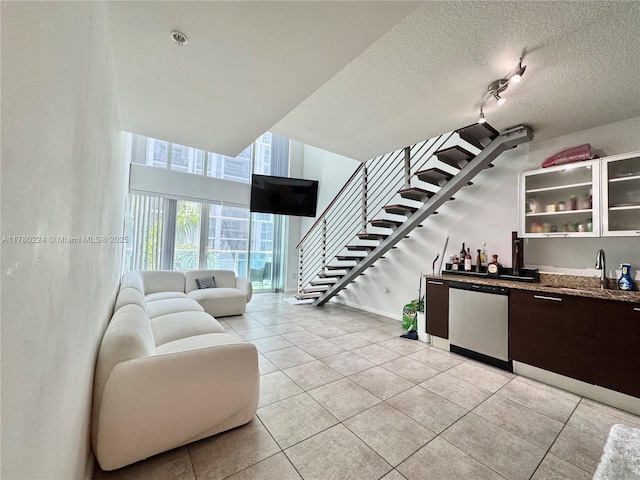 living room featuring a textured ceiling, light tile patterned floors, stairs, and indoor bar