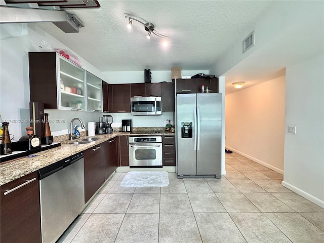 kitchen featuring light stone countertops, dark brown cabinetry, visible vents, appliances with stainless steel finishes, and a sink