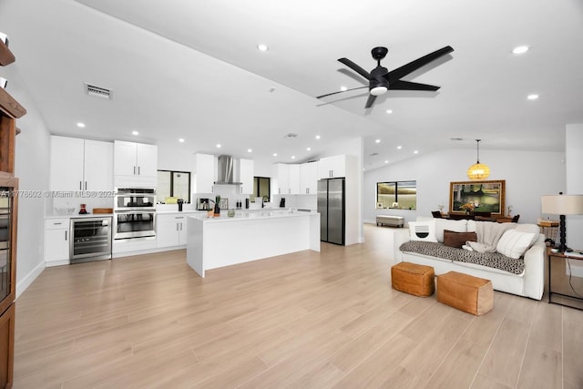 living area featuring visible vents, a ceiling fan, vaulted ceiling, light wood-style flooring, and beverage cooler