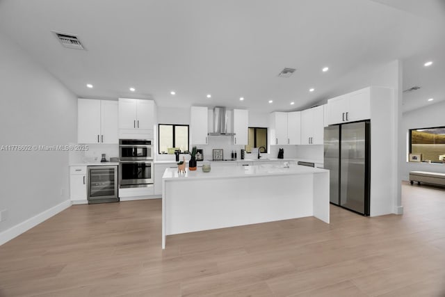 kitchen featuring appliances with stainless steel finishes, wall chimney range hood, visible vents, wine cooler, and a sink