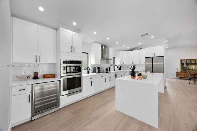 kitchen with wall chimney range hood, light countertops, wine cooler, stainless steel appliances, and a sink