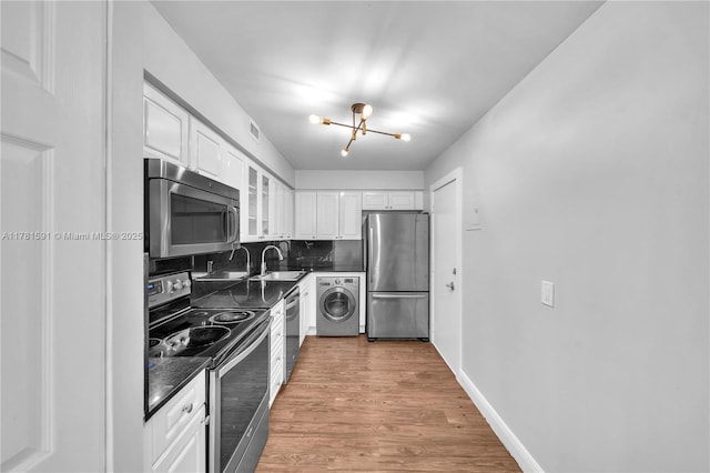 6770 Indian Creek Dr Unit 9G, Miami Beach, FL 33141 - kitchen featuring appliances with stainless steel finishes, washer / clothes dryer, dark countertops, a chandelier, and white cabinetry