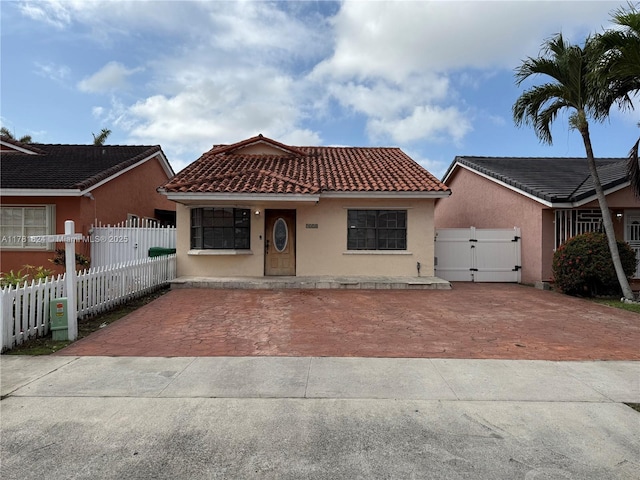 mediterranean / spanish-style house featuring a gate, fence, stucco siding, and a tile roof
