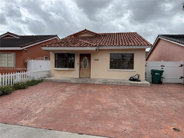 mediterranean / spanish-style house featuring stucco siding, fence, a gate, and a tile roof