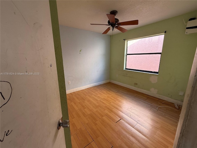 empty room featuring baseboards, wood finished floors, ceiling fan, and a wall mounted AC