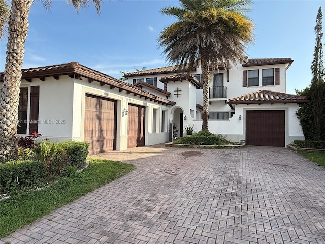 mediterranean / spanish-style house with a tile roof, an attached garage, decorative driveway, and stucco siding
