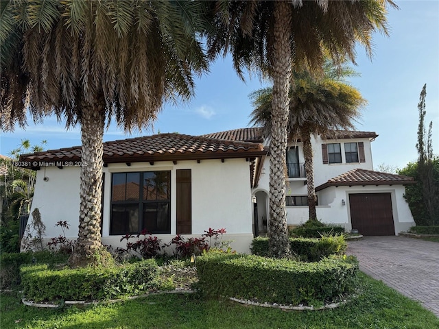 mediterranean / spanish-style home featuring a tiled roof, decorative driveway, a garage, and stucco siding