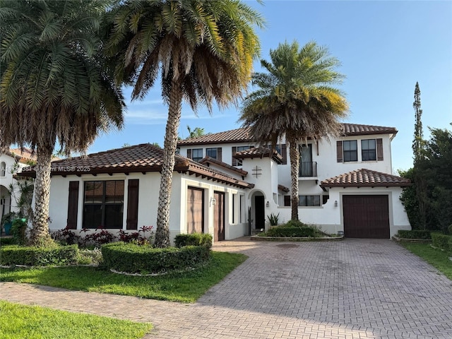 mediterranean / spanish-style home featuring a tile roof, a garage, decorative driveway, and stucco siding