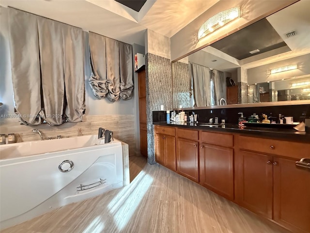 full bath featuring double vanity, a bath, visible vents, tile walls, and wood finished floors