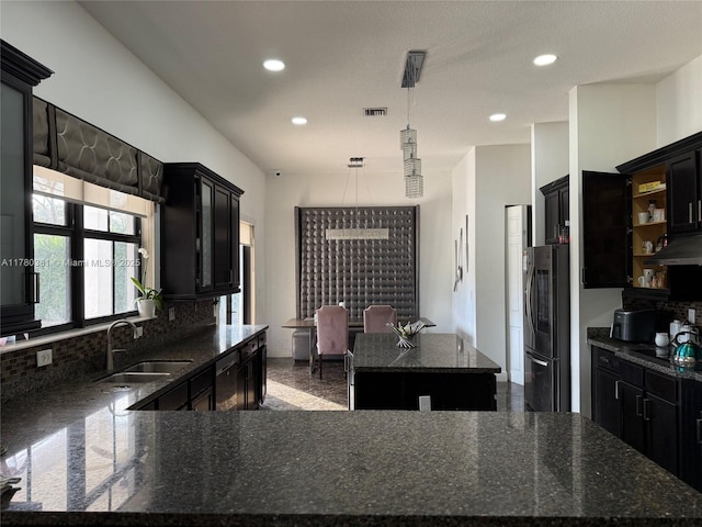 kitchen with appliances with stainless steel finishes, a center island, dark cabinetry, decorative backsplash, and a sink