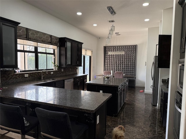 kitchen with dark cabinets, a kitchen island, dark countertops, stainless steel appliances, and a sink