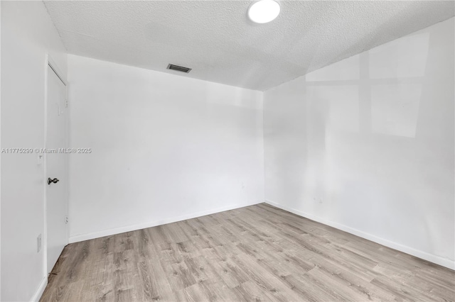 spare room with a textured ceiling, wood finished floors, baseboards, and visible vents