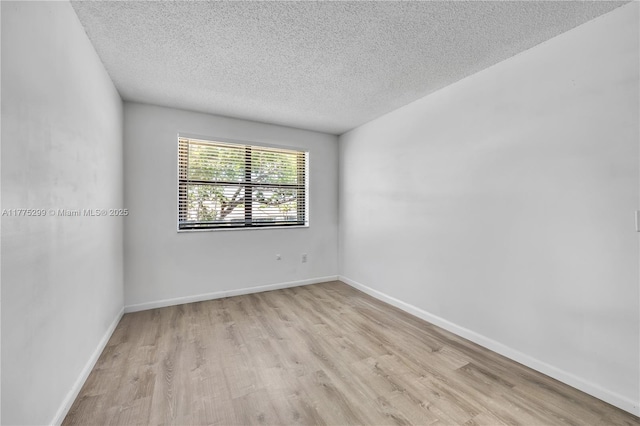 empty room featuring light wood finished floors, a textured ceiling, and baseboards