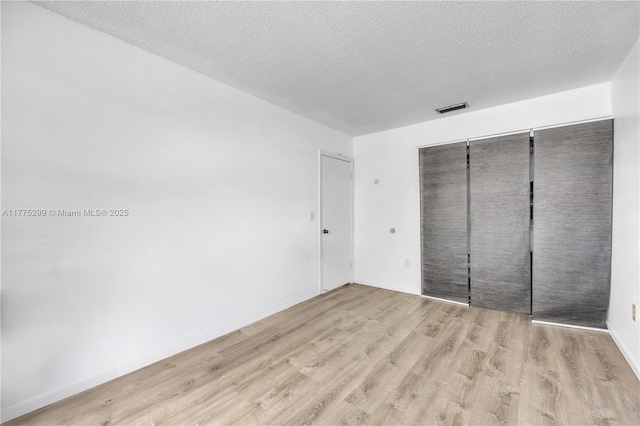 unfurnished bedroom featuring a closet, visible vents, a textured ceiling, and wood finished floors