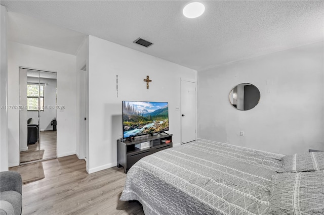 bedroom featuring visible vents, light wood-style flooring, baseboards, and a textured ceiling