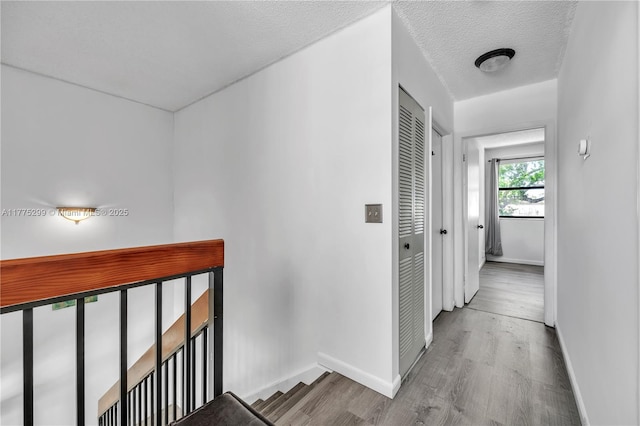 hallway featuring a textured ceiling, wood finished floors, baseboards, and an upstairs landing