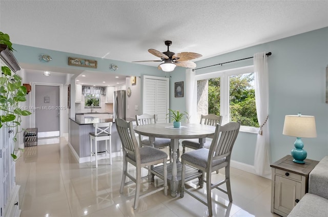 dining room featuring light tile patterned floors, ceiling fan, baseboards, and a textured ceiling