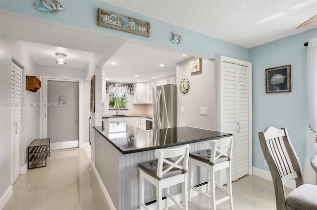 kitchen featuring white cabinets, baseboards, freestanding refrigerator, and dark countertops