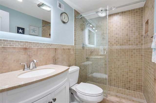 full bath featuring toilet, tiled shower, visible vents, and tile walls