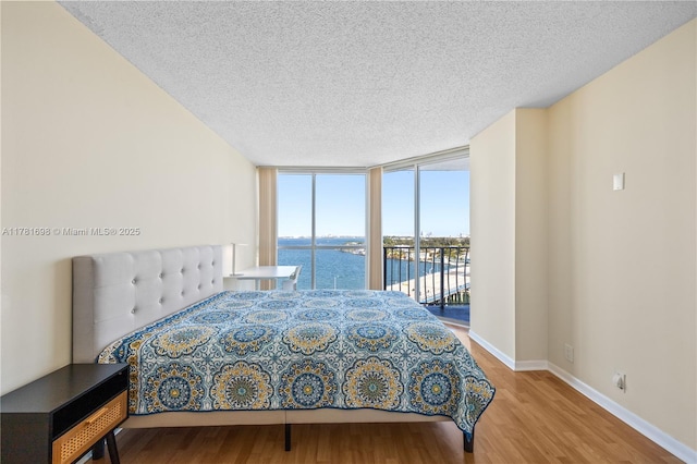 bedroom with floor to ceiling windows, access to exterior, a textured ceiling, and wood finished floors
