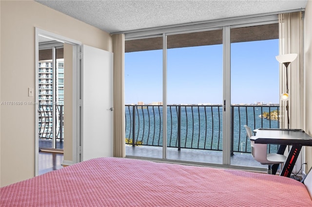 bedroom featuring a water view, expansive windows, and a textured ceiling