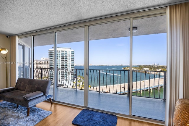 interior space with a city view, expansive windows, a textured ceiling, a water view, and wood finished floors