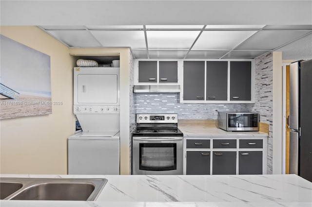 kitchen with appliances with stainless steel finishes, stacked washer / drying machine, under cabinet range hood, gray cabinets, and backsplash